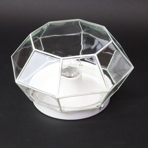 Könnte beinhalten: Weiße Deckenleuchte mit einem geometrischen Schirm aus klarem Glas.