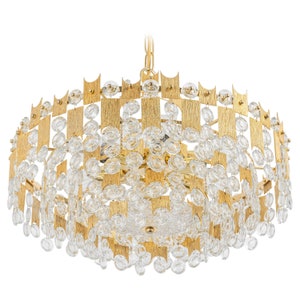 Peut inclure: Un lustre dor&eacute; avec un design g&eacute;om&eacute;trique et des accents de cristal transparent. Le lustre a une forme ronde et est suspendu &agrave; une cha&icirc;ne.
