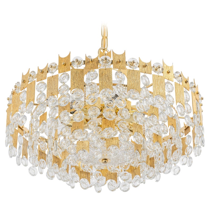 Peut inclure: Un lustre dor&eacute; avec un design g&eacute;om&eacute;trique et des accents de cristal transparent. Le lustre a une forme ronde et est suspendu &agrave; une cha&icirc;ne.