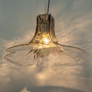 May include: A clear glass pendant light fixture shaped like a flower with a warm light shining through.