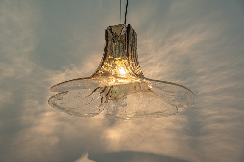 May include: A clear glass pendant light fixture shaped like a flower with a warm light shining through.