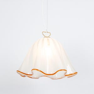 May include: White glass pendant light with a ruffled edge and a gold metal hook. The light has a warm, amber-colored trim around the edge.