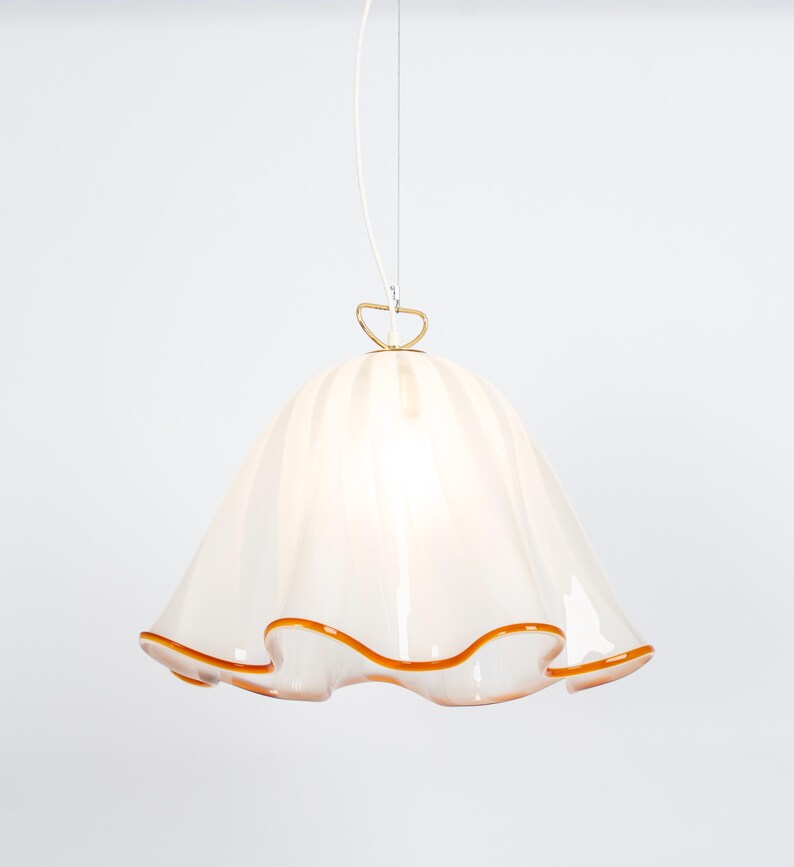 May include: White glass pendant light with a ruffled edge and a gold metal hook. The light has a warm, amber-colored trim around the edge.