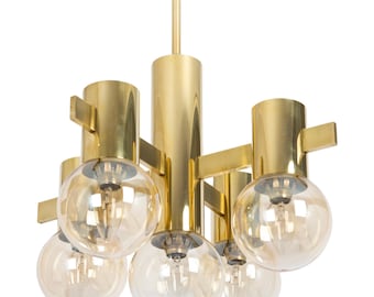 May include: A gold-toned brass chandelier with six clear glass globe light fixtures. The chandelier has a geometric design with multiple arms extending from a central column.
