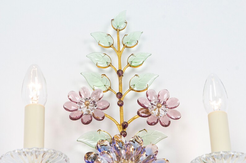 Puede incluir: Una l&aacute;mpara de pared de metal dorado con un dise&ntilde;o floral. La l&aacute;mpara tiene dos bombillas y est&aacute; decorada con flores y hojas de vidrio rosa y verde.