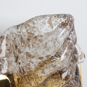 May include: A brass wall sconce with a clear glass shade. The glass has a textured, cracked ice appearance with a brown tint.