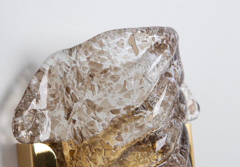 May include: A brass wall sconce with a clear glass shade. The glass has a textured, cracked ice appearance with a brown tint.