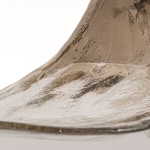May include: Close-up of a clear glass bottle with a textured surface. The bottle has a unique, curved shape.