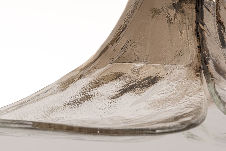 May include: Close-up of a clear glass bottle with a textured surface. The bottle has a unique, curved shape.