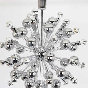 Op de afbeelding: Een chromen Sputnik-kroonluchter met meerdere bolvormige armaturen. De kroonluchter heeft een stervormig ontwerp met veel armen die zich naar buiten uitstrekken vanaf een centraal punt.