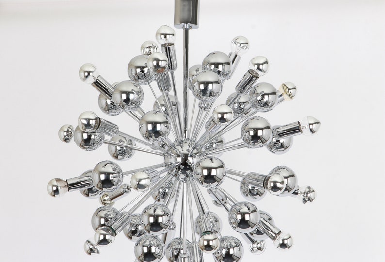 Op de afbeelding: Een chromen Sputnik-kroonluchter met meerdere bolvormige armaturen. De kroonluchter heeft een stervormig ontwerp met veel armen die zich naar buiten uitstrekken vanaf een centraal punt.