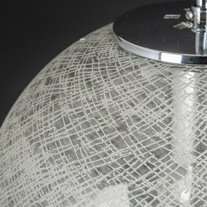 Peut inclure: Gros plan d'un luminaire suspendu en chrome et en verre. L'abat-jour en verre est textur&eacute; avec un motif en croisillons.