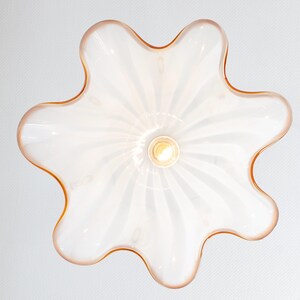 May include: A white glass ceiling light fixture with a flower-shaped design and a light bulb in the center. The fixture has a light pink rim.