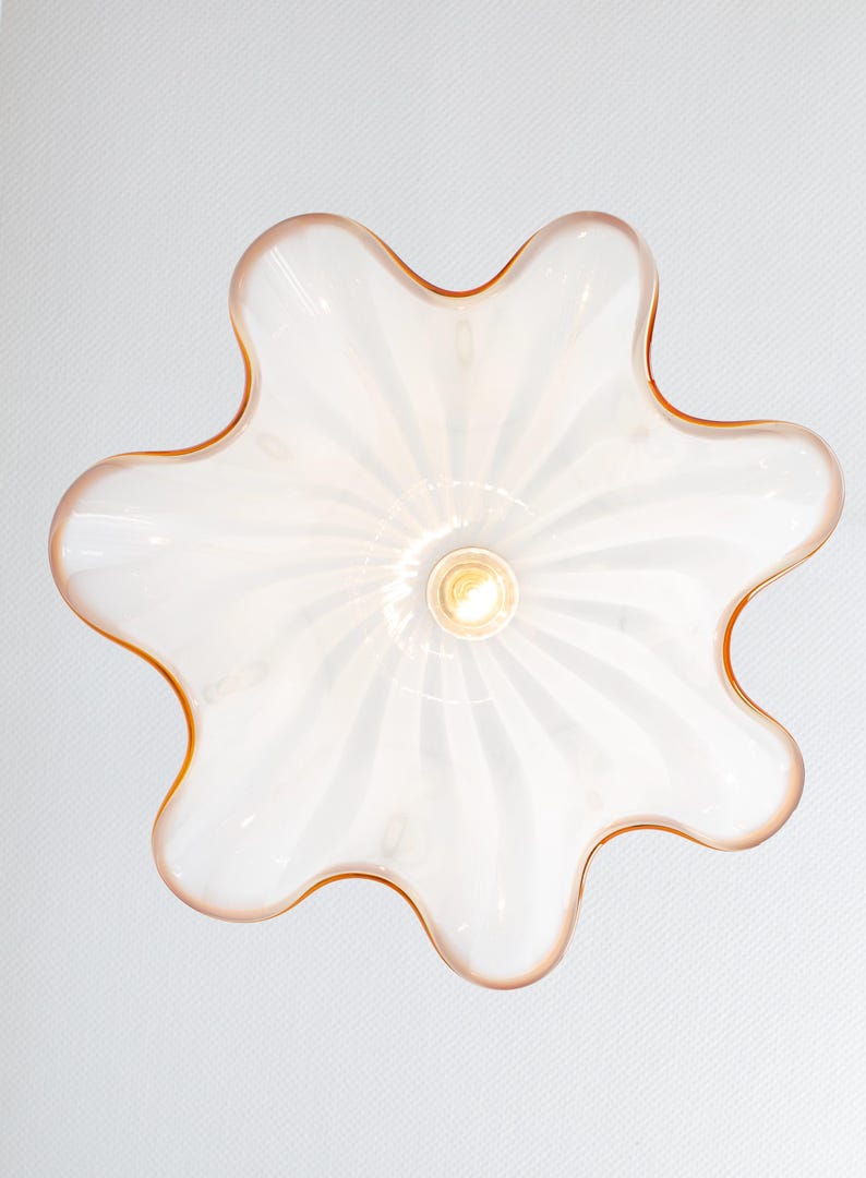 May include: A white glass ceiling light fixture with a flower-shaped design and a light bulb in the center. The fixture has a light pink rim.