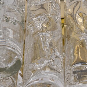 May include: Close-up of a clear glass chandelier with textured cylindrical pendants. The glass has a rippled, organic pattern.