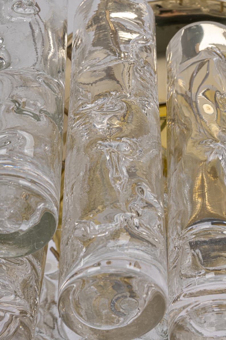 May include: Close-up of a clear glass chandelier with textured cylindrical pendants. The glass has a rippled, organic pattern.