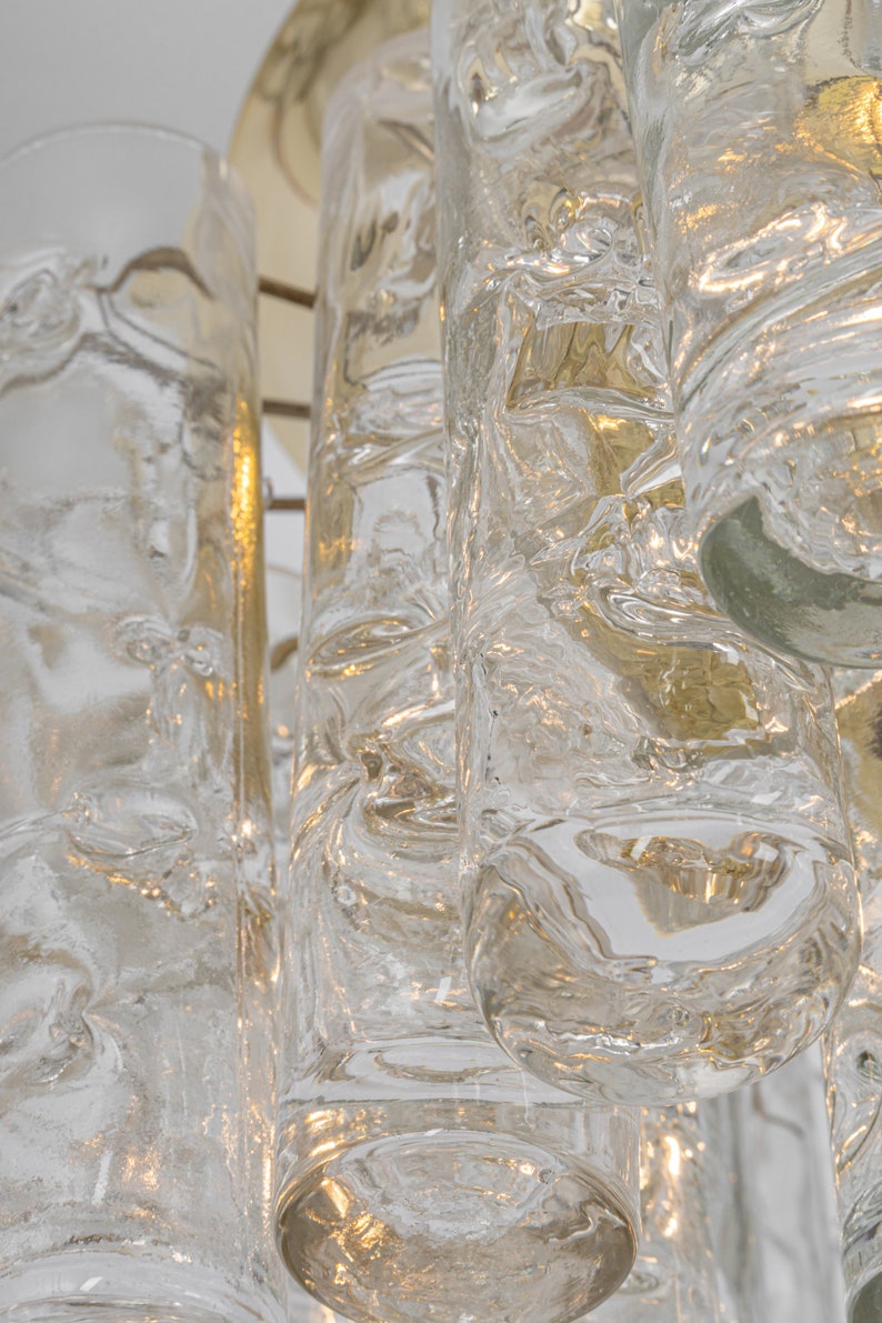 May include: A close-up of a chandelier with clear glass cylinders. The glass has a textured, bubbly appearance, and the light shines through the glass, creating a warm glow.