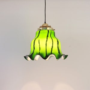 May include: A green and black striped glass pendant light with a white ruffled edge. The light fixture has a brass finish.