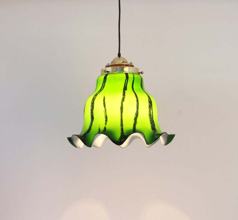May include: A green and black striped glass pendant light with a white ruffled edge. The light fixture has a brass finish.