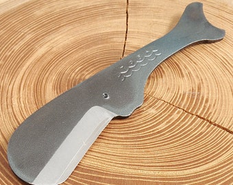 May include: A silver-colored whale-shaped razor blade with a textured surface and a wave pattern on the handle. The blade is sharp and has a slight curve.
