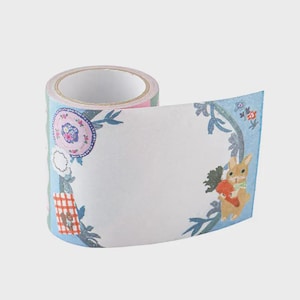 Puede incluir: Un rollo de cinta washi decorativa con un diseño caprichoso. La cinta tiene un fondo azul claro con ilustraciones de un conejito con una zanahoria, flores y un plato. Ideal para scrapbooking y manualidades.