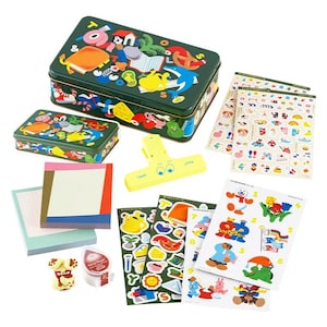 Può includere: Una scatola di metallo verde con illustrazioni colorate di animali, oggetti e lettere. La scatola contiene un set di adesivi colorati, una clip di plastica gialla e un set di note di carta colorate.