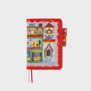 Può includere: Una copertina per taccuino rettangolare con bordo rosso e motivi floreali bianchi. Il centro mostra l'illustrazione di un edificio a più piani con varie stanze, mobili colorati e piccoli animali. Un passante rosso per penna si trova sul lato.