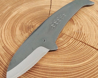 May include: A gray metal knife with a whale-shaped handle and a wavy design. The knife is sharp and has a pointed tip.