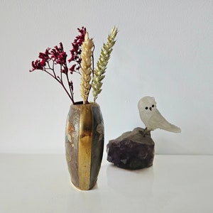 May include: A small, decorative vase with a brass and brown finish, holding dried red and tan flowers. A small, white owl figurine sits on a purple amethyst crystal, creating a natural, artistic display.