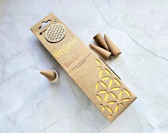 May include: A brown cardboard box of organic sandalwood incense cones, with a wooden accent and cut-out floral designs. The text on the box reads "Organic Sandalwood 12 Jumbo Incense Cones & Burner."