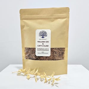以下が含まれることがあります： 茶色のクラフト紙袋で、茶色のハーブブレンドが見える透明な窓が付いています。袋には「YELLOW UXI & CAT'S CLAW」の文字と木のロゴが入った白いラベルが付いています。乾燥した葉の小枝が袋の前にあります。