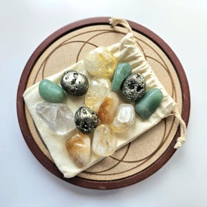 Pu&ograve; includere: Una collezione di pietre preziose lucide in vari colori, tra cui giallo, verde e trasparente, esposta su un sacchetto beige con coulisse. Il sacchetto poggia su un vassoio circolare in legno con bordo marrone scuro e design inciso. Le pietre preziose variano per dimensioni e forma.