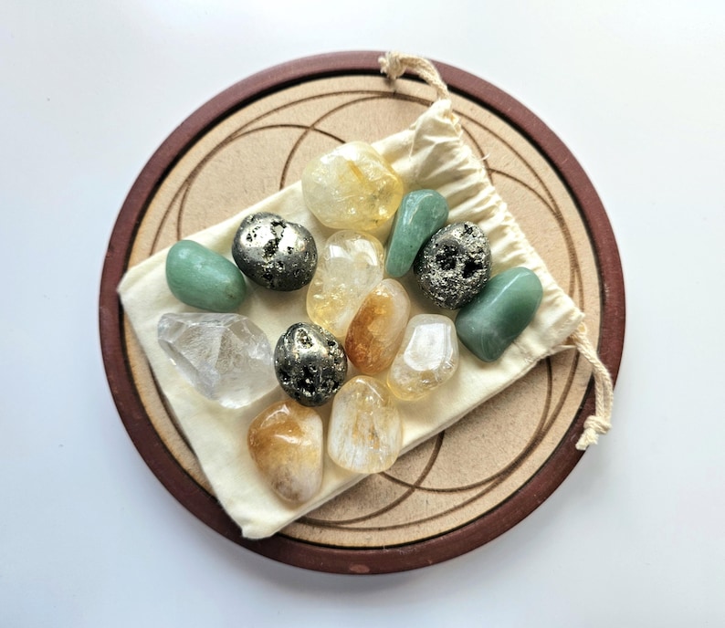 Pu&ograve; includere: Una collezione di pietre preziose lucide in vari colori, tra cui giallo, verde e trasparente, esposta su un sacchetto beige con coulisse. Il sacchetto poggia su un vassoio circolare in legno con bordo marrone scuro e design inciso. Le pietre preziose variano per dimensioni e forma.