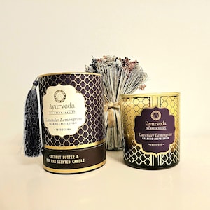 Pode incluir: Duas velas perfumadas com o texto "Ayurveda Lavender Lemongrass" em um design dourado e roxo. Uma vela está em uma caixa cilíndrica com uma borla, e a outra é um pote de vidro. As velas são de manteiga de coco e cera de soja.