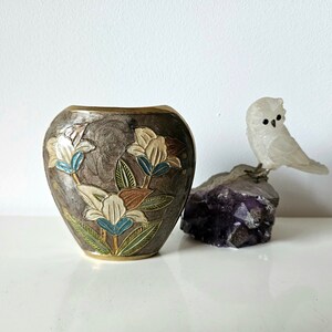 May include: A decorative vase with a floral design in shades of white, blue, and brown. The vase is next to a carved white owl perched on a purple crystal. The vase has a metallic finish.