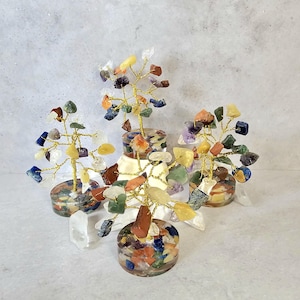 Peut inclure: Plusieurs arbres de pierres précieuses avec des branches en fil d'or et des feuilles de pierres colorées. Les arbres sont placés dans des bases en résine remplies de diverses pierres. Des cristaux de quartz clair sont placés autour des bases.