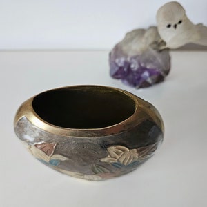 May include: Oval-shaped, dark brown metal bowl with a gold rim. The bowl features a floral design in shades of brown, beige, and blue. A small, white owl figurine sits atop a purple crystal formation in the background.