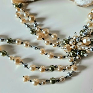 May include: A vintage-style necklace featuring multiple strands of faux pearls in cream, silver, and olive green hues. The necklace has a central cluster of pearls and a delicate, cascading design, perfect for adding a touch of elegance to any outfit.