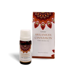 Könnte beinhalten: Eine kleine braune Glasflasche mit reinem Aromaöl aus Ceylon-Zimt mit weißem Verschluss, neben einer passenden Schachtel. Die Schachtel und die Flasche weisen ein dekoratives Mandala-Design in Rot-, Orange- und Goldtönen auf. Der Text auf der Flasche und der Schachtel lautet "Sri Lankan Cinnamon Pure Aroma Oil".