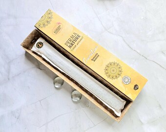 May include: A rectangular box of Perma Nature incense, with a gold and brown design. The box is open, revealing a long, wrapped bundle of incense sticks. The box has the words "Perma Nature" and "Signature" printed on it.