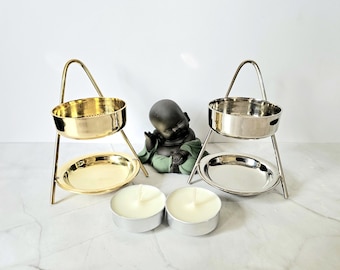 Könnte beinhalten: Zweistöckige Metall-Kerzenhalter, einer goldfarben und einer silberfarben, mit einer kleinen Buddha-Statue und zwei weißen Teelichtkerzen. Die Kerzenhalter haben einen runden Sockel und eine perforierte obere Schale.