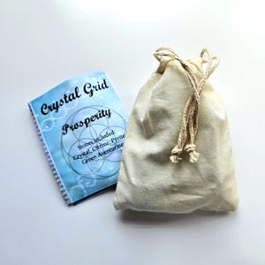 Pu&ograve; includere: Un libretto azzurro con le parole "Crystal Grid Prosperity" accanto a un sacchetto beige con coulisse. Il libretto elenca le pietre incluse: Cristallo, Citrino, Pirite e Avventurina verde. La borsa &egrave; in tessuto color naturale.