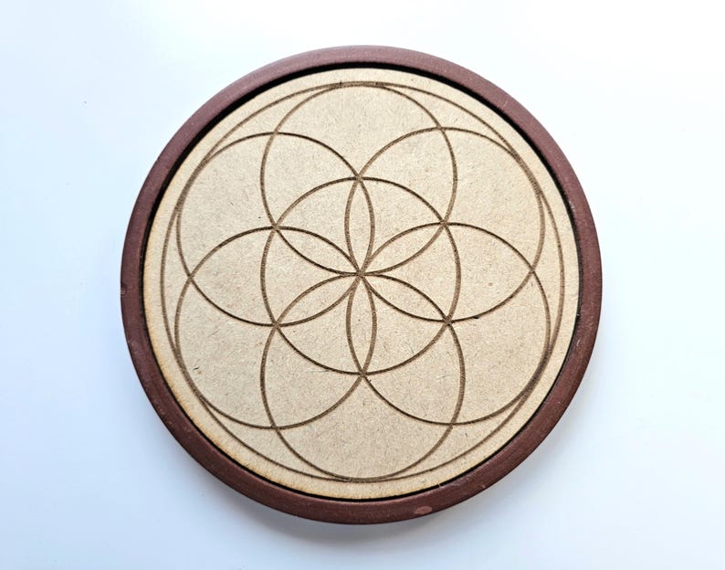 Pu&ograve; includere: Un sottobicchiere rotondo in legno con un bordo marrone scuro e un centro marrone chiaro. Il centro presenta un design tagliato al laser di cerchi sovrapposti, creando un motivo geometrico. Il sottobicchiere &egrave; progettato per l'uso con tazze e bicchieri.