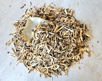 Puede incluir: Un montón de virutas de madera de color marrón claro con algunos trozos más oscuros y una hoja pálida y translúcida. Las virutas de madera están esparcidas sobre una superficie de color claro, creando una apariencia natural y texturizada.