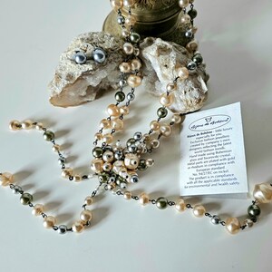 May include: A necklace and matching earrings featuring a mix of pearl colors: cream, gray, and olive green. The necklace has a central cluster of pearls and a delicate chain. The earrings are small, round, and gray. A tag is visible.