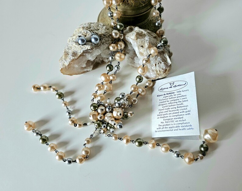 May include: A necklace and matching earrings featuring a mix of pearl colors: cream, gray, and olive green. The necklace has a central cluster of pearls and a delicate chain. The earrings are small, round, and gray. A tag is visible.