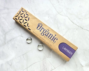May include: A rectangular box of "Organic Goodness" masala incense sticks in a light brown color. The box has a purple label that says "Lavender". The box has a decorative cut-out pattern on the top. Two clear glass marbles are next to the box.