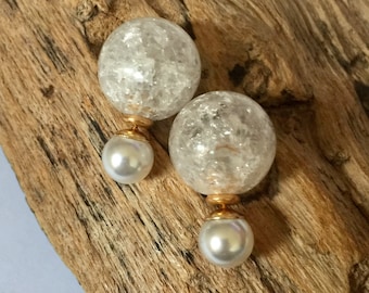 May include: A pair of double-sided earrings. Each earring features a large, clear, crackled glass orb on top, connected to a smaller, white, pearlescent orb with a gold-colored metal post. The earrings are displayed on a piece of weathered wood.