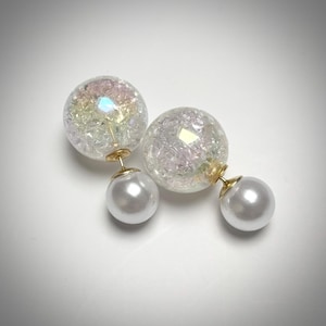 Può includere: Un paio di orecchini a doppia faccia. La parte anteriore di ogni orecchino è una sfera trasparente e strutturata con accenti iridescenti. Il retro è una sfera bianca perlacea, collegata da un perno color oro.