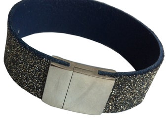May include: A black leather bracelet with a silver magnetic clasp. The bracelet is covered in small, sparkly gold glitter.